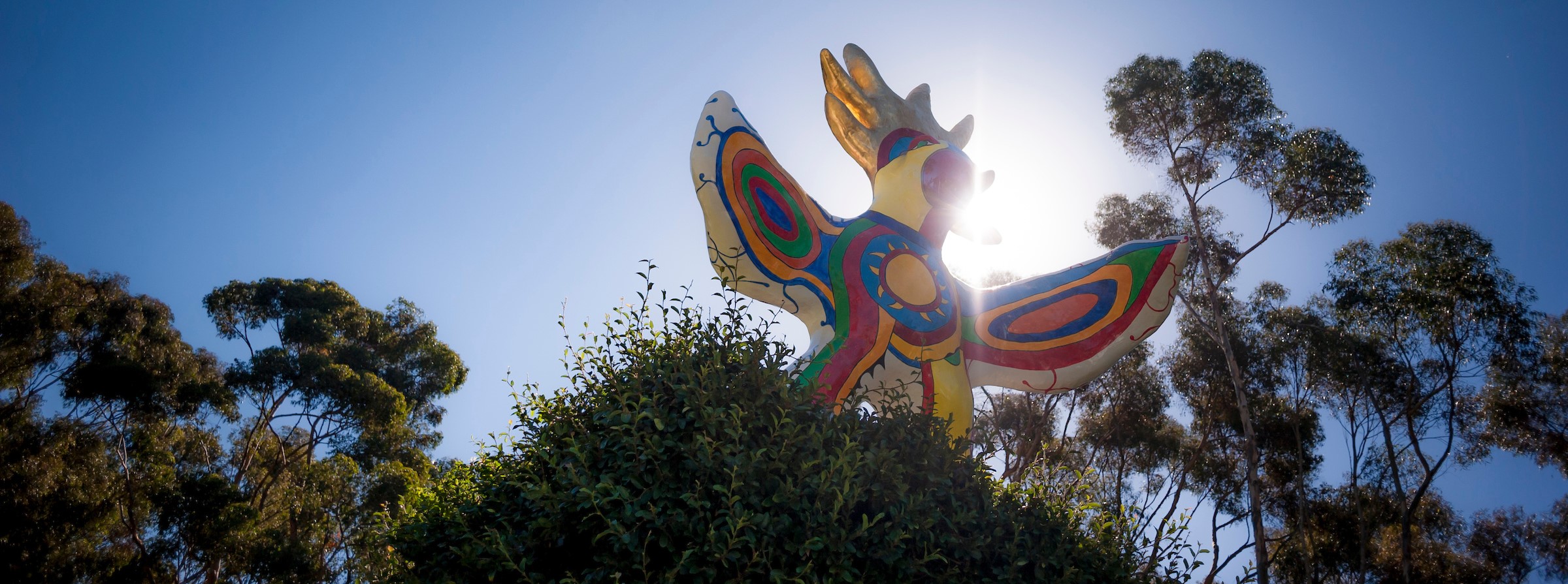 The colorful Sun God statue, with green trees and a blue sunny sky in the backdrop
